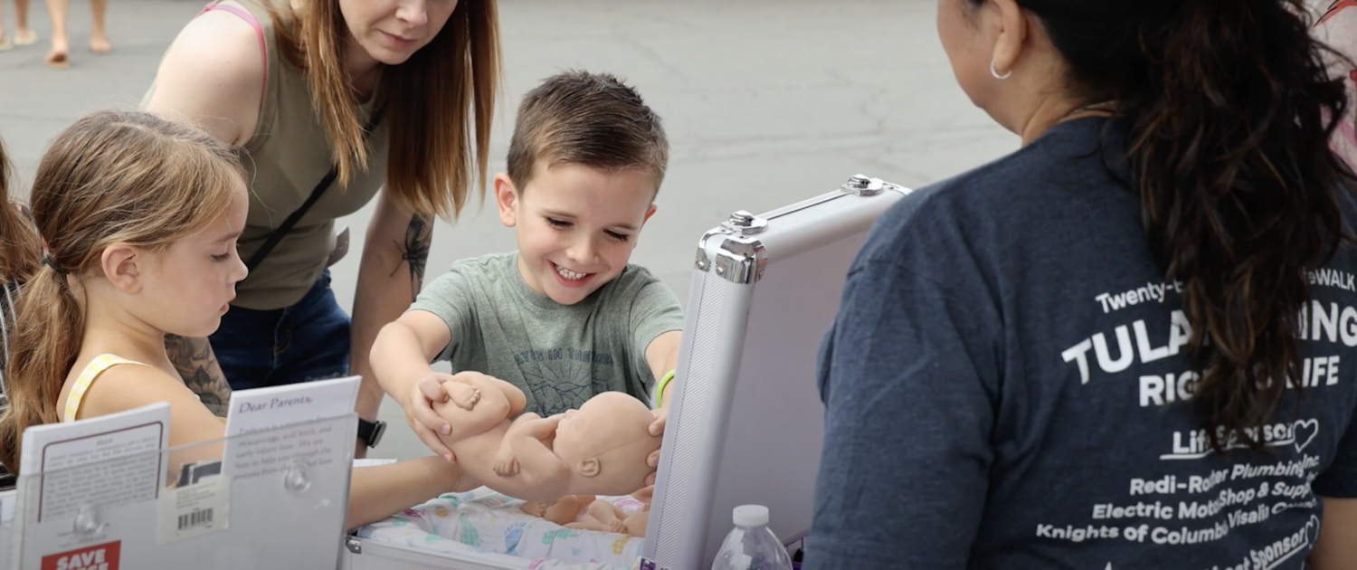 A mom watches as her two kids hold a model fetus at a Tulare-Kings Right to Life display.